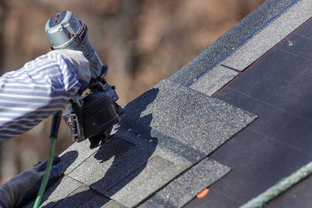 Rain falls on a roof above an insulated attic while a homeowner checks the ceiling below.